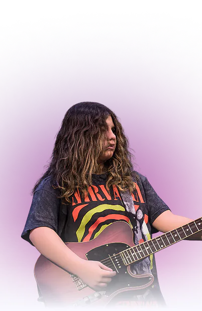 Young person with long wavy hair playing an electric guitar against a purple gradient background, wearing a vintage Nirvana band t-shirt.